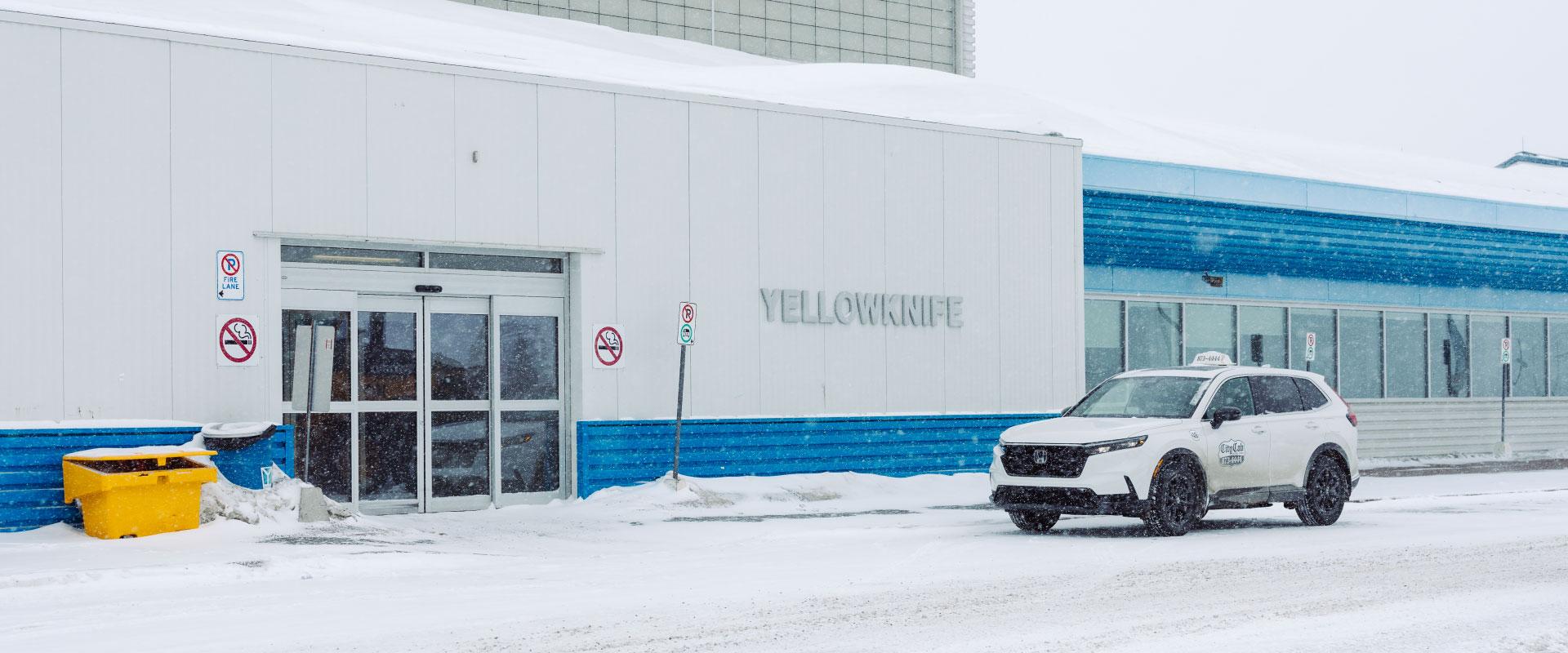 The image features a taxi parked in front of Yellowknife Airport. 